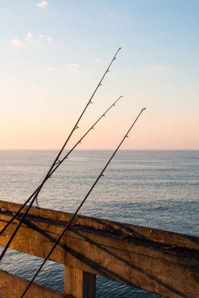 Three fishing poles resting on pier with ocean background and clouds.