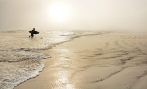 Man  with surfboard on the beautiful foggy beach.