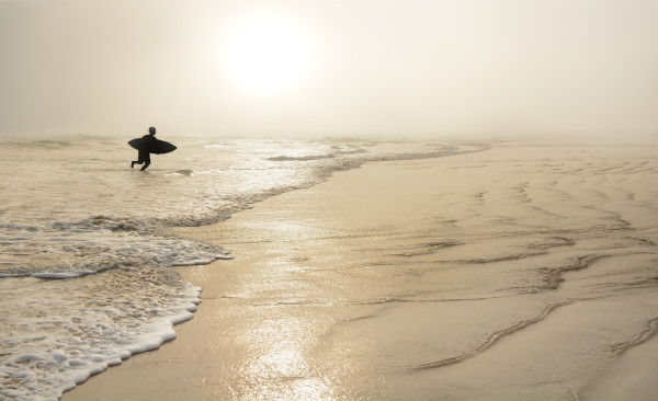 Man  with surfboard on the beautiful foggy beach.