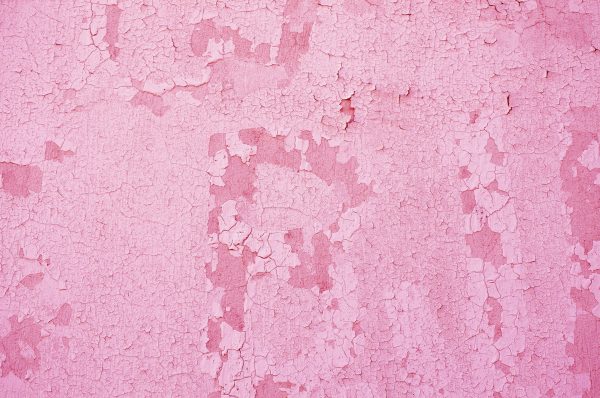 Fragment of old house wall close-up. Pink background. Peeling plaster on concrete surface. Cracks in paint. Copy space. Place for text. Selective focus image.